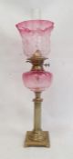 Cranberry and brass oil lamp having panelled flared shade, cranberry well, on reeded column,