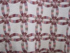 Modern patchwork quilt in pinks and maroons on a white ground and a small circular sewing basket (