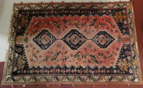 A Persian carpet with triple hooked central medallions with stylised bird motifs on the madder