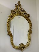 A DECORATIVE GILTWOOD CARVED WALL MIRROR, the shaped glass set within a carved Rococo style frame