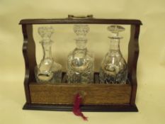 A VINTAGE OAK THREE BOTTLE TANTALUS WITH SEVEN DECANTER LABELS