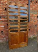 A SIXTEEN DRAWER OAK HABERDASHERY UNIT WITH CUPBOARD BELOW, the drawers being glazed with brass hand