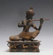 A TIBETAN TYPE BRONZE FIGURE OF A DEITY PLAYING A FLUTE, sat upon a forest with deer being chased by
