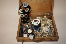 A PINE LIDDED BOX CONTAINING COSTUME JEWELLERY AND WRISTWATCHES TO INCLUDE A COLLECTION OF BROOCHES