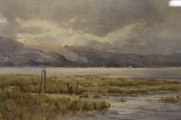 A FRAMED AND GLAZED WATERCOLOUR DEPICTING A MOUNTAINOUS RIVER LANDSCAPE WITH SHEEP GRAZING SIGNED