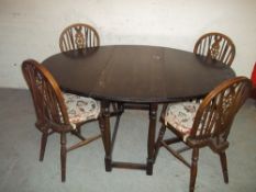 AN ANTIQUE OAK DROP LEAF DINING TABLE WITH FOUR WHEEL BACK CHAIRS IN THE ERCOL STYLE