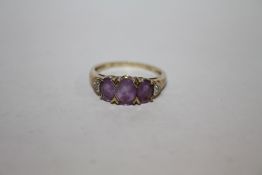 A HALLMARKED 9K GOLD THREE STONE AMETHYST DRESS RING WITH DIAMOND CHIPS TO THE SHOULDERS APPROX