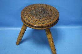 A CARVED OAK THREE LEGGED STOOL