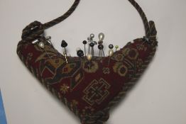 A SMALL COLLECTION OF WHITE METAL HAT PINS ON A HEART SHAPED PIN CUSHION