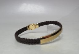 A DESIGNER STYLE YELLOW METAL AND PLAITED LEATHER BRACELET, stamped 18K to magnetic / hinged