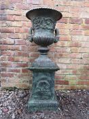 A VICTORIAN STYLE CAST METAL SHAPED GARDEN URN, raised on plinth, with twin handles and foliate