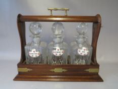 A TWENTIETH CENTURY MAHOGANY THREE DECANTER TANTALUS, with three ceramic decanter labels, with