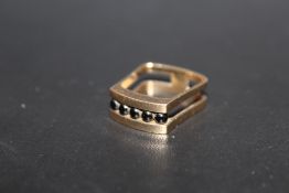 A HALLMARKED 9 CARAT GOLD UNUSUAL SHAPED RING, set with five polished black spherical stones in a