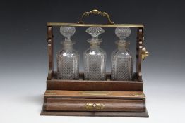 AN OAK THREE BOTTLE TANTALUS WITH DRAW, W 34.75 cm