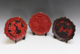 THREE ORIENTAL CINNABAR WALL PLAQUES / CABINET PLATES, varying colour ways, Dia. 23 cm (3)