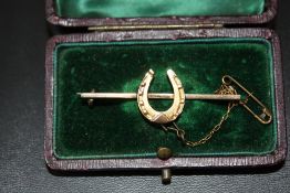 A 9 CARAT GOLD HORSESHOE BAR BROOCH, with steel pin and safety chain, approx weight 3.8g, W 5 cm