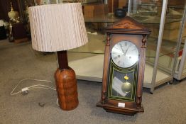 A TURNED WOODEN TABLE LAMP TOGETHER WITH A REPRODUCTION LEGEND WALL CLOCK, LAMP HEIGHT WITH SHADE 68