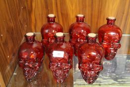 SIX RED GLASS SKULL DECANTERS