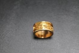 AN UNMARKED YELLOW METAL BAND, decorated text all around, approx weight 8.4g, ring size K 1/2