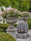 A pair of continental carved limestone garden urns on plinths