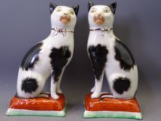 STAFFORDSHIRE POTTERY CATS - a pair, black and white with separate front legs on rust cushion bases,