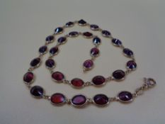 ITALIAN 18CT GOLD & GARNET NECKLACE of 29 facet cut stones, oval mounted with looped ends, 44cms
