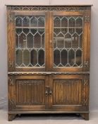 JAYCEE OAK BOOKCASE CUPBOARD having carved and linenfold detail with twin leaded glazed upper