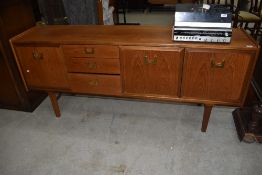 A vintage teak long john style sideboard, with brass drop handles, label removed from drawer (coin