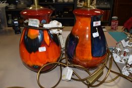 A pair of Poole pottery lamp bases in reds, oranges and blues having a slightly lustrous finish.