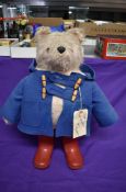 A Gabrielle Designs plush covered Padding Bear soft toy, wearing blue jacket and red wellingtons,