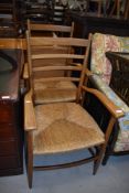 A pair of vintage ladder back carver chairs, having rush seats, possibly teak