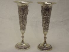 Two Indian white metal bud vases having embossed decoration depicting deities, no marks, one rim