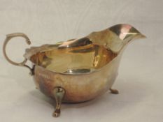 A silver sauce boat having trefoil pad feet, loop handle and shaped rim, Birmingham 1948, Adie