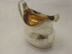 A Georgian silver cream jug of helmet form having engraved and bright cut decoration with crest to