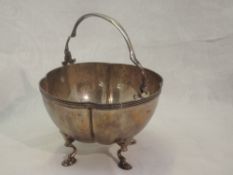 An Edwardian silver sugar bowl of shaped form having quatrefoil hoof feet and swing handle, London