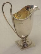 An Edwardian silver cream jug of plain helmet form having reided loop handle and square platform