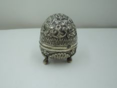 A white metal pounce pot of egg form having trefoil scallop and bun feet, repousse floral and scroll