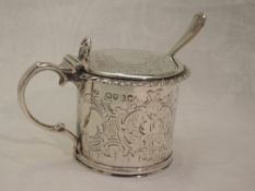 A Victorian silver mustard pot of drum form having engraved decoration, hinged lid and blue glass