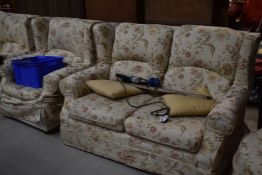 A set of two settees and arm chair with floral covers, and similar circular footstool