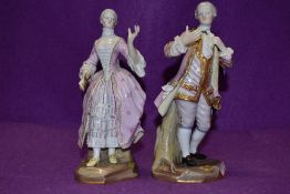A pair of Meissen figurines of gentleman and companion, the gent is wearing a pink frock coat with