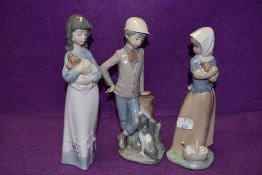 Three Lladro Nao figurines, two girls with puppies and a boy with dog at his feet.