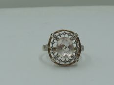 A lady's dress ring having a morganite style oval stone within an open border having diamond chip