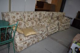 A set of two settees and arm chair with floral covers, and similar circular footstool