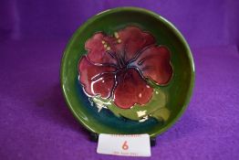 A Moorcroft pin dish having red hibiscus to green ground., impressed signature to underside.