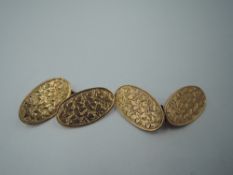 A pair of Edwardian 9ct gold cufflinks of oval form having engraved foliate decoration and chain