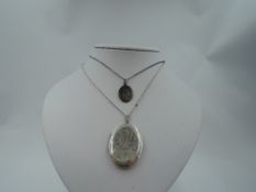An oval white metal locket stamped silver bk & fnt having engraved scroll decoration on a white