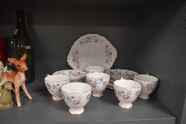 A collection of mid century cups, saucers,cake plate and more, having pink rose pattern and gilt