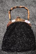 A early 20th century black beaded evening bag having ornate carved fastening and bamboo handle.