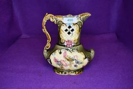 A unusually shaped jug having cut work to front and floral design on green ground in the majolica