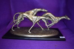 A figure base of three exaggerated racing grey hounds or similar race dogs cast in a heavy brass